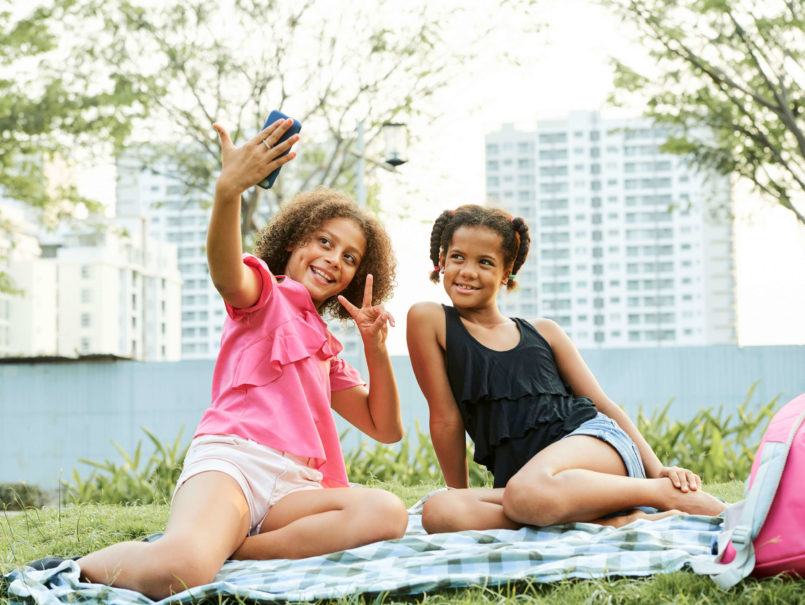 snapchat parental control - two young teen girls taking a selfie sitting on the grass in a park in a city