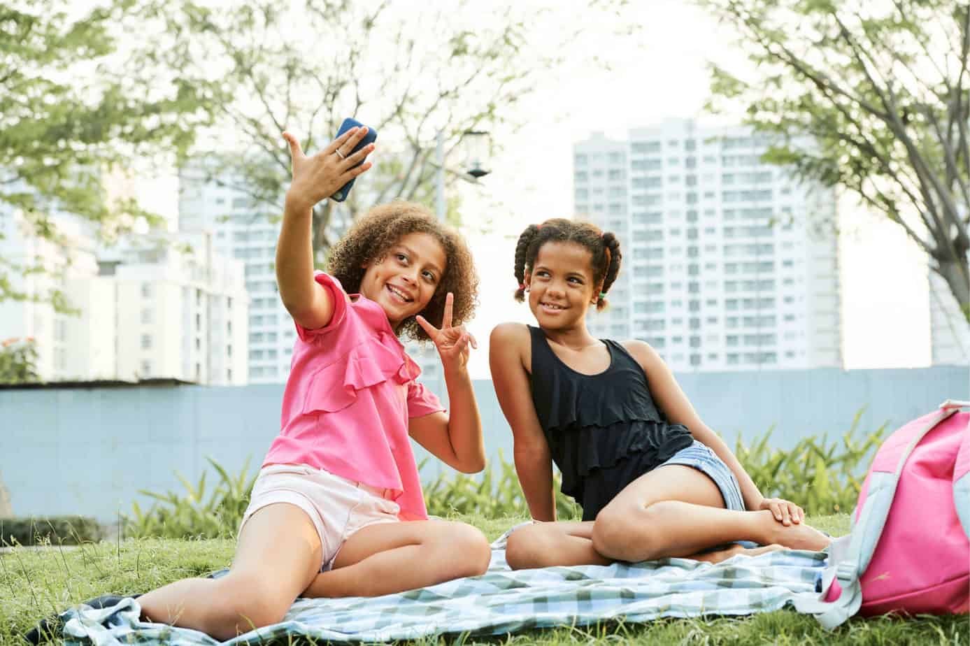 snapchat parental control - two young teen girls taking a selfie sitting on the grass in a park in a city